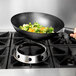 A hand using a Winco wok ring to cook vegetables in a wok on a stove.