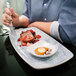 A person eating a rectangular platter of food with a fork.