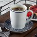A Schonwald stone saucer with blue ornaments holding a cup of coffee and a plate of fruit.