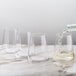 A person pouring white wine into a Stolzle stemless wine glass on a table.