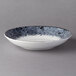 A white porcelain deep coupe plate with a black speckled rim.