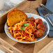 A Schonwald Structure Blue porcelain deep coupe plate with pasta and meatballs, a knife and fork on a blue cloth.