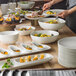 A table with rectangular white porcelain dishes full of food.