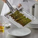 A person holding a Choice quarter size aluminum bun pan filled with asparagus