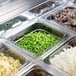 A Turbo Air stainless steel sandwich prep table with trays of food on a counter.