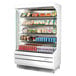 A white Turbo Air refrigerated air curtain merchandiser with food on shelves.