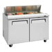 A Turbo Air stainless steel refrigerated sandwich prep table on a brown surface.