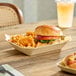 A rectangular molded fiber tray containing a sandwich and curly fries on a wooden table.