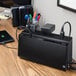 A black APC Back-UPS device on a desk with cords plugged into it.