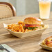 A rectangular molded fiber tray filled with a sandwich and curly fries on a wooden table.