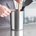 A person holding Tablecraft brushed stainless steel utensil holder with a knife and wooden spoon inside.