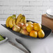 A black G.E.T. Enterprises Bugambilia rectangular fruit bowl with a bowl of fruit and utensils on a table.