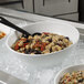 A white G.E.T. Enterprises Bugambilia resin-coated aluminum bowl of food on a table with a spoon.