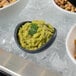 A G.E.T. Enterprises Bugambilia granite black resin-coated aluminum bowl of guacamole and nuts on a table.