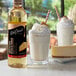 A bottle of DaVinci Gourmet Classic Cheesecake flavoring syrup next to a glass of milk.