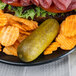 A plate with a sandwich, potato chips, and a Nathan's Famous Kosher Dill Pickle.