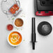 A Vitamix blender with a bowl of soup and spices on a counter in a professional kitchen.