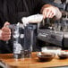 A man pouring ice into a Vitamix blender on a counter with a bowl of brown liquid.