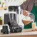 A man pouring brown liquid into a Vitamix blender.