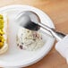 A person using a Vollrath stainless steel scoop to serve potato salad on a plate.