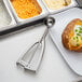 A baked potato with cheese and green onions with a Vollrath stainless steel scoop.