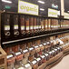 A store with a shelf filled with Rosseto triple cereal dispensers filled with different types of dry food.