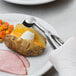 A gloved hand using a Vollrath stainless steel squeeze handle disher to scoop a potato.