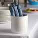 A white round melamine utensil holder with blue napkins inside.