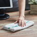 A hand using a green striped Choice bar towel to wipe a wooden table.