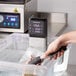 VacPak-It SV08 sous vide immersion circulator head in a plastic container of water with tongs.