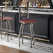 A metal bar stool with a cross back design, swivel feature, and a mahogany wood seat.