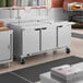 A large stainless steel, three-door mega top refrigerated sandwich prep table on wheels.