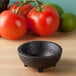 A black charcoal polypropylene Pequeno molcajete on a wood surface with tomatoes and a lime.
