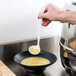 A hand holding a white Fineline Platter Pleasers disposable ladle over a bowl of soup.