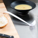 A bowl of soup and a spoon on a cutting board.