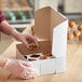 A person putting a blueberry muffin in a 9" x 9" x 4" white mini cupcake / muffin box.