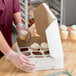 A white cupcake or muffin box with a 12-slot reversible insert being filled with cupcakes by a person wearing gloves.