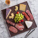 A G.E.T. Enterprises Bugambilia mocha resin-coated aluminum square disc with rim holding cheese and grapes on a marble surface.