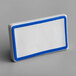 A white rectangular ceramic table tent sign with a blue border and decal.