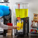 A woman using a Narvon 5 gallon refrigerated beverage dispenser to pour yellow liquid into a cup.