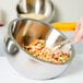 A person using tongs to serve food from a stainless steel American Metalcraft double wall bowl.