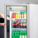 A person opening a Beverage-Air white glass door refrigerator to get a drink.