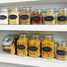 A shelf with jars of food including lentils, pasta, beans, almonds, pistachios, and more. The jars have black oval chalkboard labels.