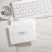 A white desk with a white keyboard and Avery silver rectangle foil return address labels on white envelopes.