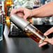 A hand pouring a drink into a Vollrath stainless steel tumbler on a counter.