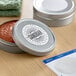 A round metal container with a white label on a table with a jar of red sauce and a paper towel.