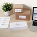 A box of white Avery shipping labels on a stack of white paper next to a laptop.