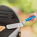 A person using a Dexter-Russell blue perforated turner to grill meat.