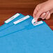 A person's hand putting a white Avery filing label on a blue file folder.