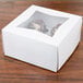 A white box with a clear window holding 4 chocolate cupcakes.